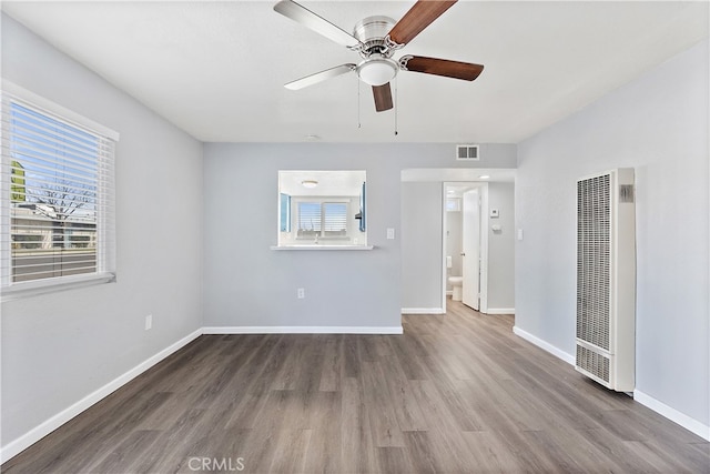 spare room with baseboards, visible vents, a heating unit, and wood finished floors