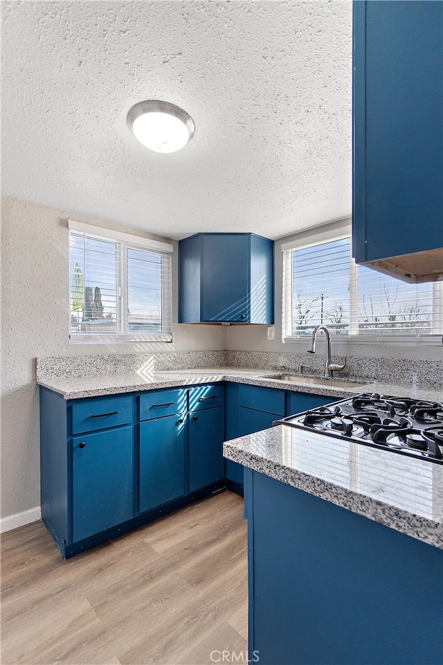 kitchen featuring a textured wall, blue cabinetry, a sink, and light wood-style flooring