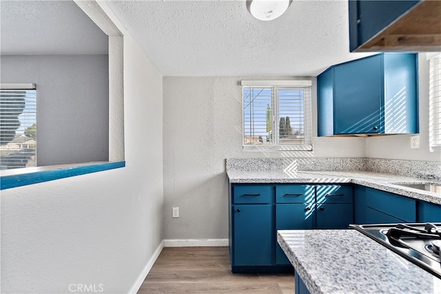 kitchen with baseboards, a textured wall, light countertops, light wood-type flooring, and blue cabinetry