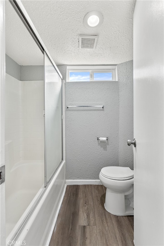 full bath with visible vents, a textured wall, toilet, wood finished floors, and a textured ceiling