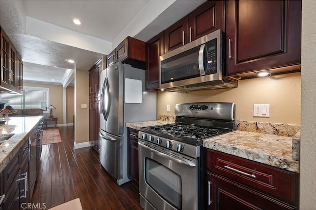 kitchen featuring baseboards, appliances with stainless steel finishes, light stone countertops, dark wood finished floors, and glass insert cabinets