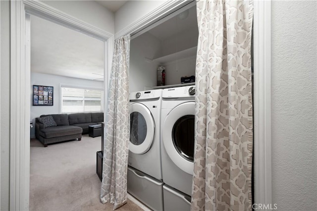 washroom with a textured wall, laundry area, washing machine and clothes dryer, and light colored carpet