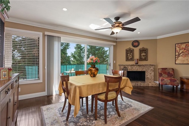 dining area featuring baseboards, a ceiling fan, dark wood-type flooring, crown molding, and a fireplace