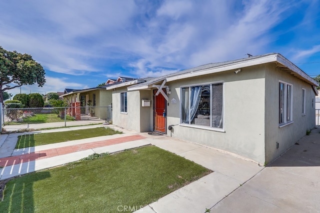 view of front of home featuring fence, a front lawn, and stucco siding