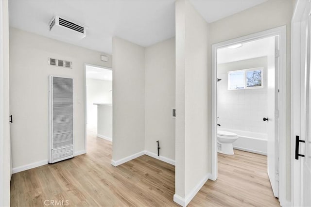 corridor featuring light wood-style floors, a heating unit, visible vents, and baseboards