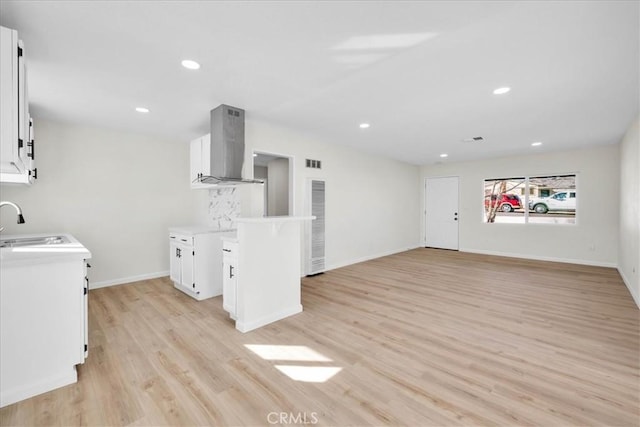 kitchen with island exhaust hood, light countertops, light wood-style flooring, open floor plan, and white cabinetry