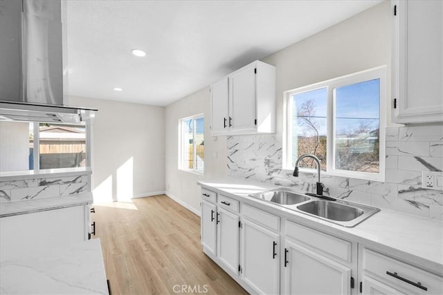 kitchen with baseboards, decorative backsplash, white cabinets, light wood-type flooring, and a sink