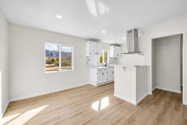 kitchen with light countertops, backsplash, white cabinetry, island range hood, and light wood-type flooring