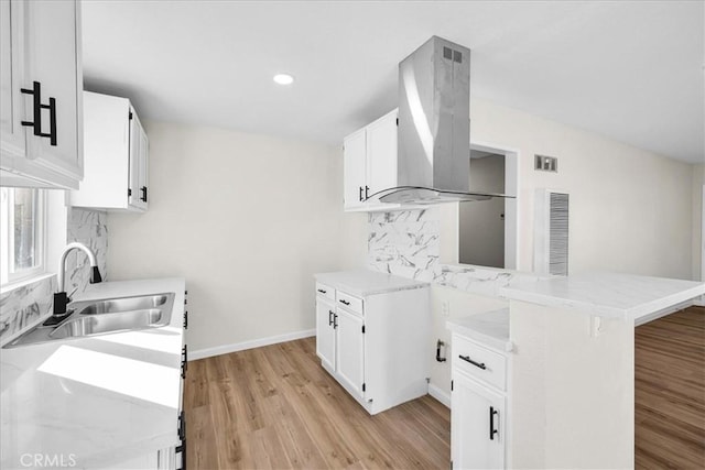 kitchen featuring a sink, light countertops, island exhaust hood, and white cabinetry