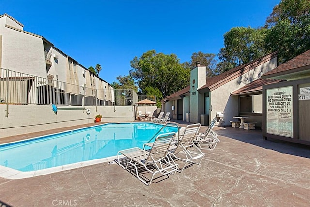 community pool with a patio area, fence, and a residential view