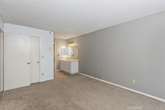 unfurnished bedroom with baseboards, light colored carpet, ensuite bathroom, a textured ceiling, and a closet