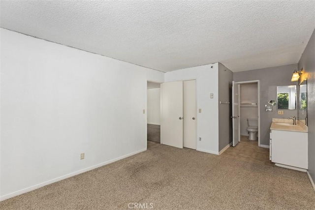 unfurnished bedroom with light colored carpet, a sink, a textured ceiling, and baseboards