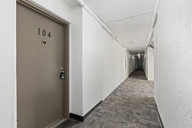 hall with dark colored carpet and a textured wall