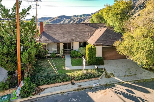 view of front of house featuring roof with shingles, a chimney, concrete driveway, a mountain view, and a front lawn