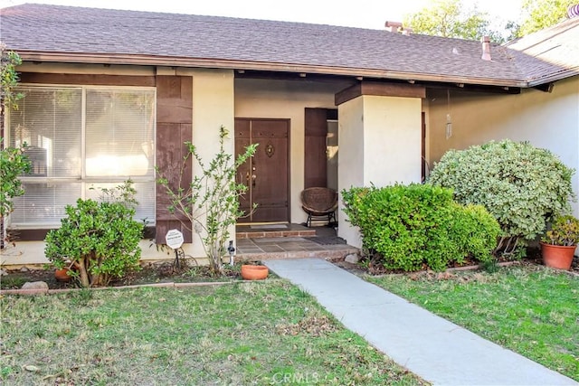 property entrance with stucco siding, a lawn, and roof with shingles