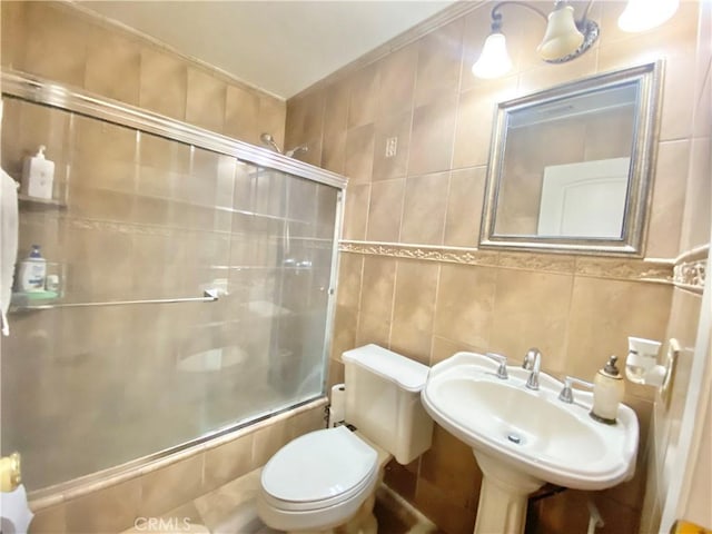 bathroom with a sink, enclosed tub / shower combo, toilet, and tile walls