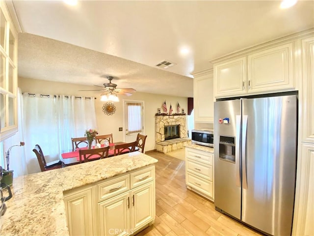 kitchen featuring light stone counters, a fireplace, stainless steel appliances, light wood-style flooring, and a ceiling fan