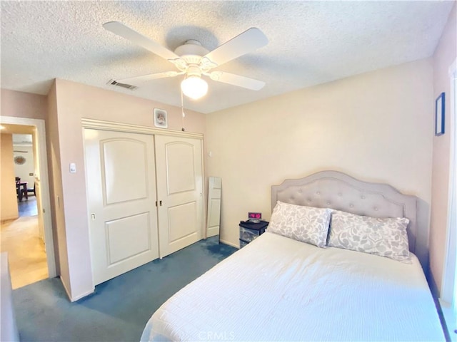 bedroom featuring a textured ceiling, ceiling fan, visible vents, a closet, and dark colored carpet