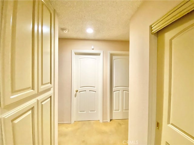 corridor with a textured ceiling and light colored carpet