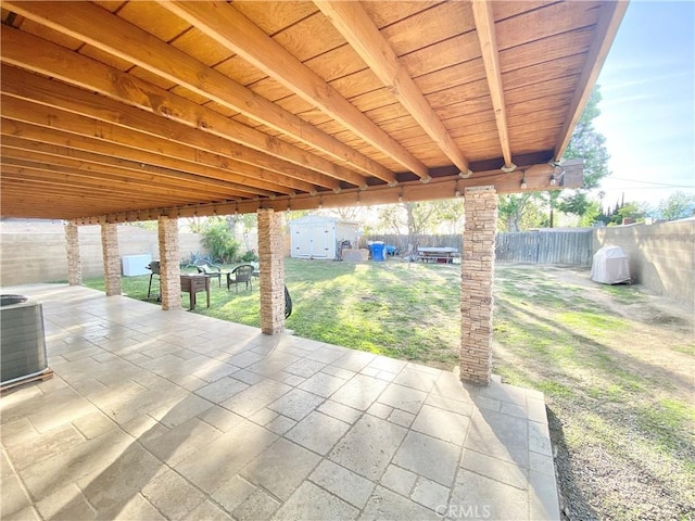 view of patio featuring central air condition unit, a fenced backyard, a storage unit, and an outbuilding