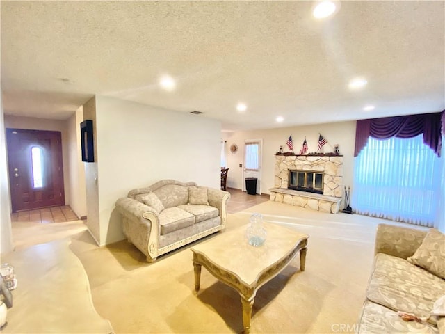 living area featuring visible vents, a textured ceiling, a stone fireplace, a wealth of natural light, and recessed lighting