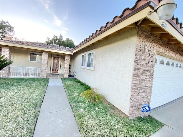 entrance to property with a garage, stone siding, a tiled roof, a lawn, and stucco siding