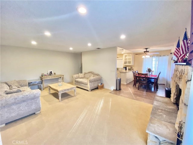 living area with a stone fireplace, a ceiling fan, and recessed lighting