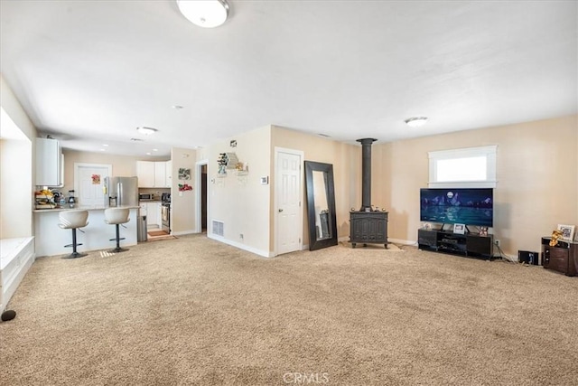 living room featuring light carpet, visible vents, a wood stove, and baseboards