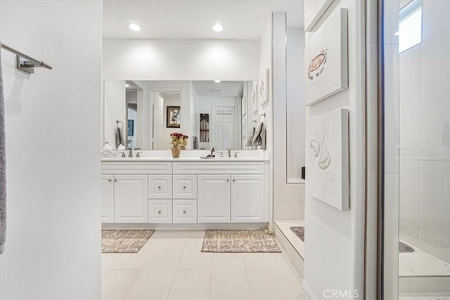 bathroom with tile patterned flooring, a sink, a tile shower, and double vanity