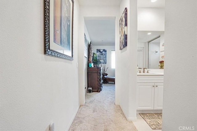 hallway featuring light carpet, a sink, and baseboards