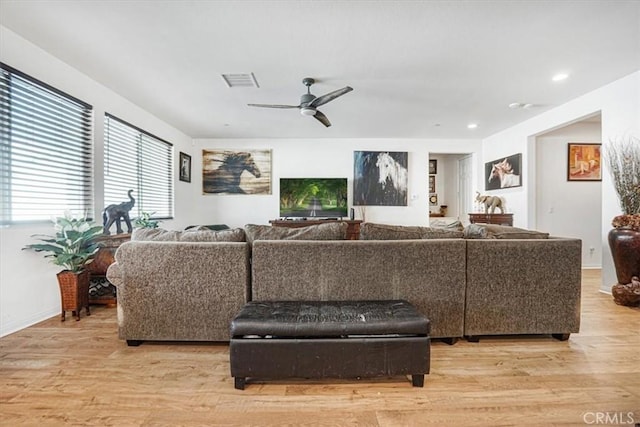 living room featuring baseboards, light wood-style flooring, visible vents, and a ceiling fan