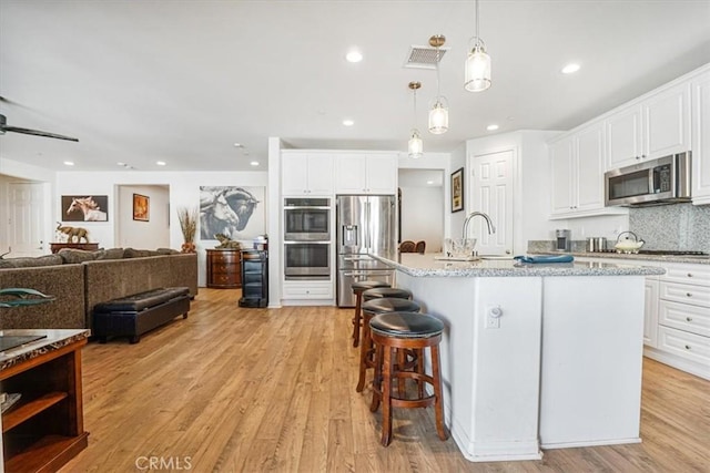 kitchen with stainless steel appliances, an island with sink, white cabinetry, and decorative light fixtures