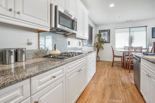 kitchen with stone counters, light wood-style floors, white cabinets, appliances with stainless steel finishes, and decorative backsplash