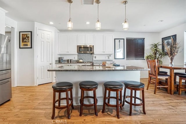 kitchen featuring white cabinets, dark stone counters, appliances with stainless steel finishes, hanging light fixtures, and light wood-type flooring