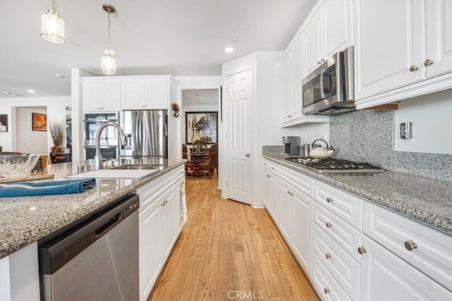 kitchen with light stone counters, appliances with stainless steel finishes, white cabinetry, and decorative light fixtures