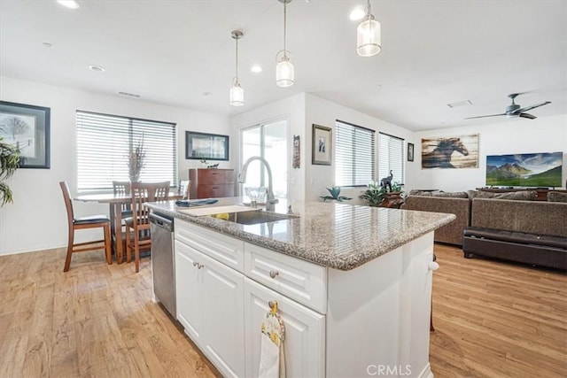 kitchen featuring open floor plan, a kitchen island with sink, a sink, white cabinetry, and dishwasher