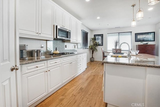 kitchen with stainless steel appliances, a sink, white cabinetry, and decorative light fixtures