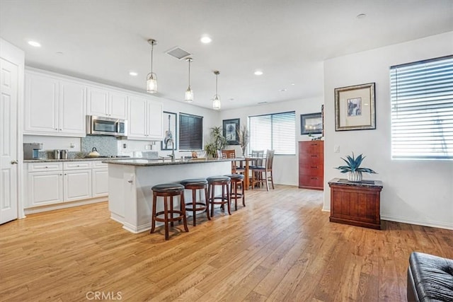 kitchen featuring a breakfast bar, a center island with sink, stainless steel microwave, hanging light fixtures, and white cabinetry