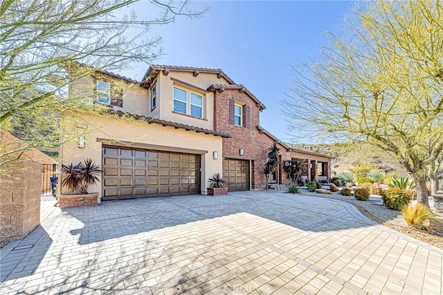 mediterranean / spanish home featuring decorative driveway, a tiled roof, an attached garage, and stucco siding