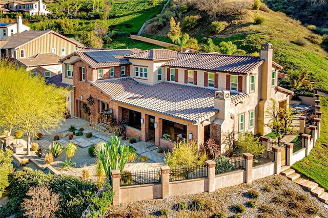 back of property featuring fence private yard, a chimney, roof mounted solar panels, and a tiled roof