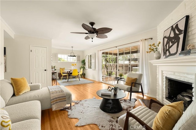 living area featuring baseboards, ceiling fan, ornamental molding, a fireplace, and wood finished floors