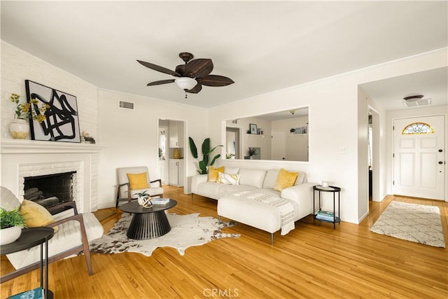 living area with a ceiling fan, a brick fireplace, wood finished floors, and visible vents