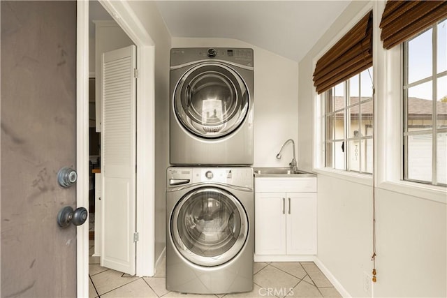 laundry room featuring light tile patterned floors, baseboards, cabinet space, a sink, and stacked washer and dryer