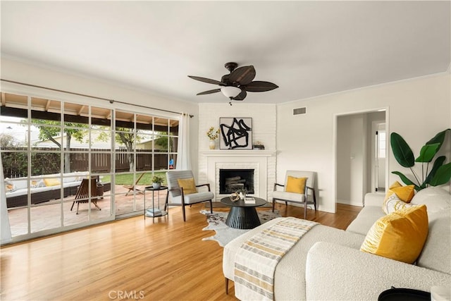 living area with light wood finished floors, visible vents, a fireplace, and a ceiling fan