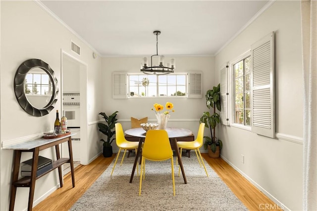 dining space featuring light wood-style flooring, a healthy amount of sunlight, visible vents, and ornamental molding