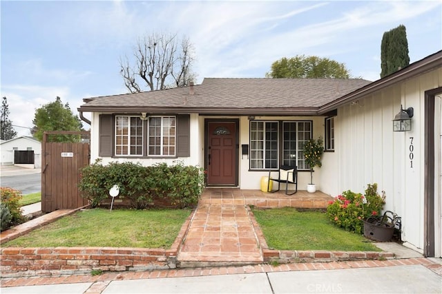 view of front facade with covered porch, a shingled roof, and a front lawn