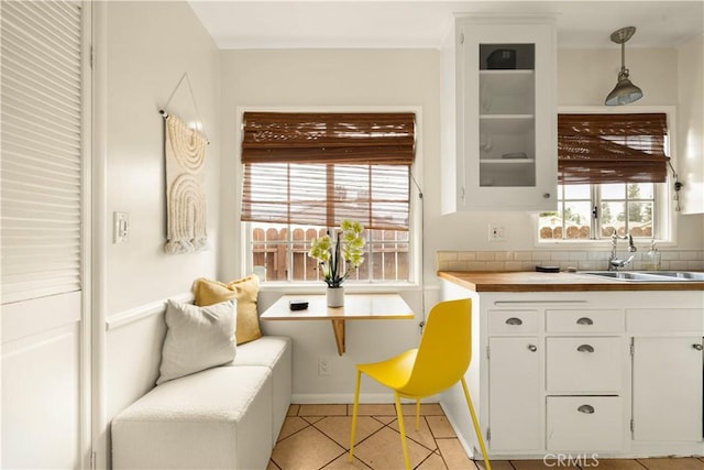 kitchen with glass insert cabinets, light tile patterned floors, hanging light fixtures, white cabinetry, and a sink