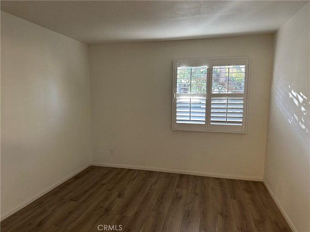 empty room featuring dark wood-style flooring and baseboards