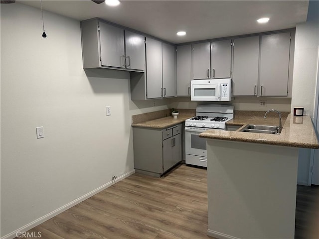 kitchen featuring white appliances, light wood finished floors, a peninsula, gray cabinets, and a sink