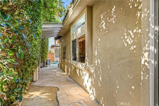 view of side of home featuring a patio area, stucco siding, fence, and a pergola